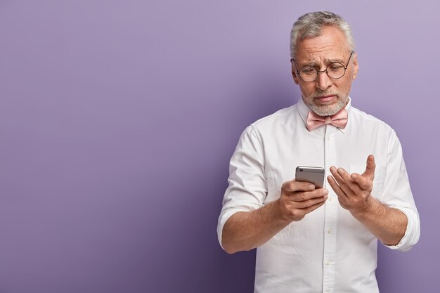 Homem sênior de camisa branca e gravata borboleta rosa segurando o telefone