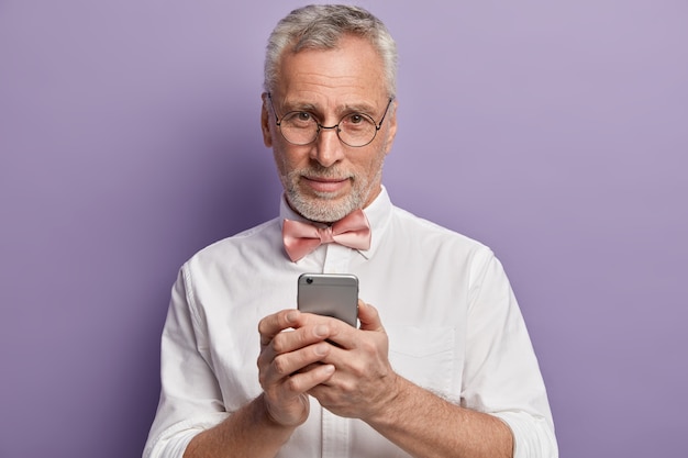 Homem sênior de camisa branca e gravata borboleta rosa segurando o telefone