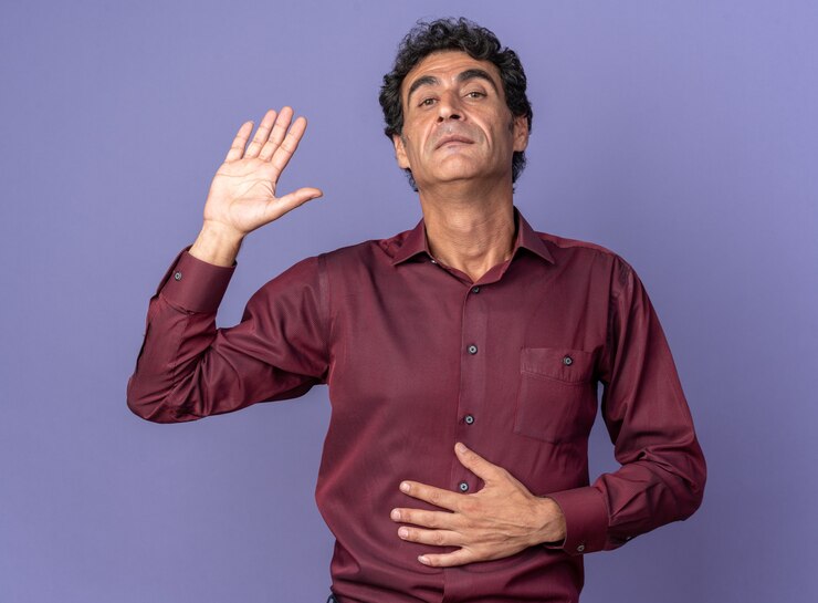 Foto grátis homem sênior de camisa roxa olhando para a câmera, levantando a mão e parecendo confiante