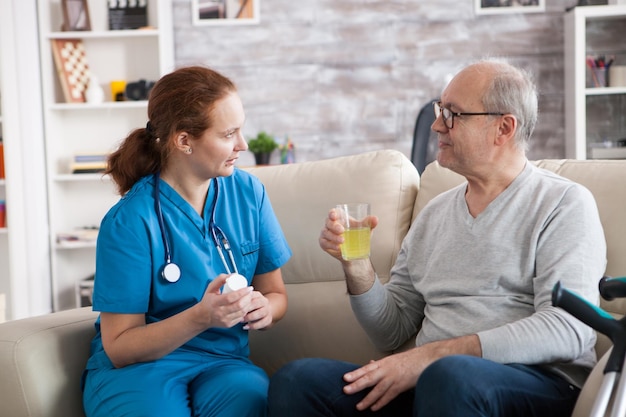 Homem sênior e senhora enfermeira conversando em um lar de idosos. Homem de idade idosa tomando seus comprimidos.