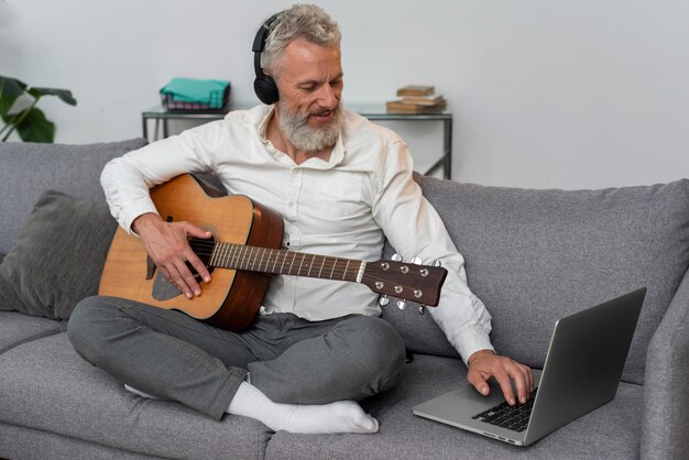 Homem sênior em casa no sofá usando laptop para estudar aulas de violão