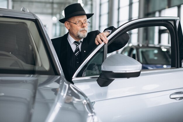 Homem sênior em um showroom de carro, escolhendo um carro