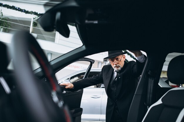 Homem sênior em um showroom de carro, escolhendo um carro