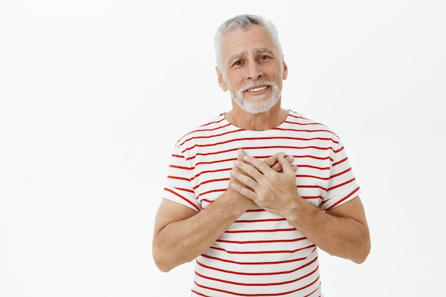 Homem sênior emocionado e feliz, lisonjeado de mãos dadas no coração e sorrindo