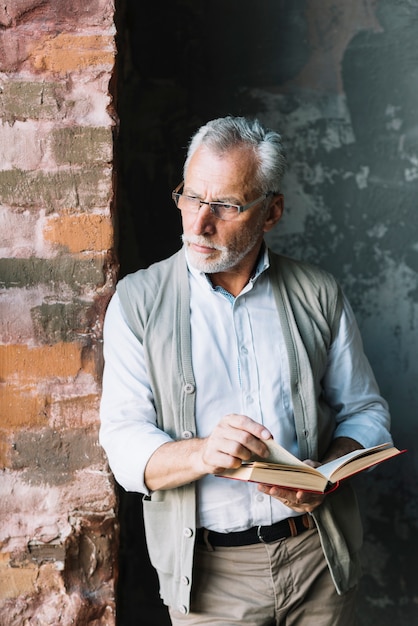 Foto grátis homem sênior, inclinar-se, parede tijolo, segurando, livro