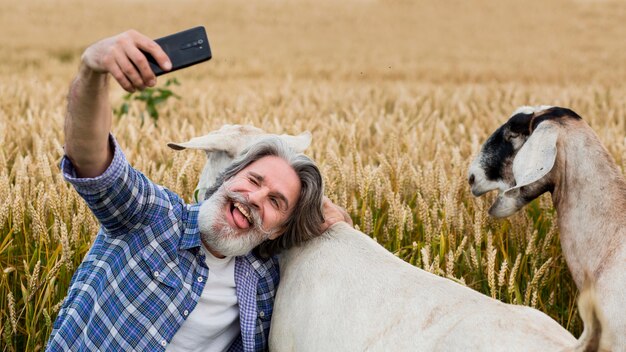 Homem sênior pegando slefie com cabra