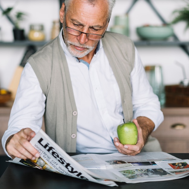 Foto grátis homem sênior, segurando, maçã verde, em, mão, jornal leitura