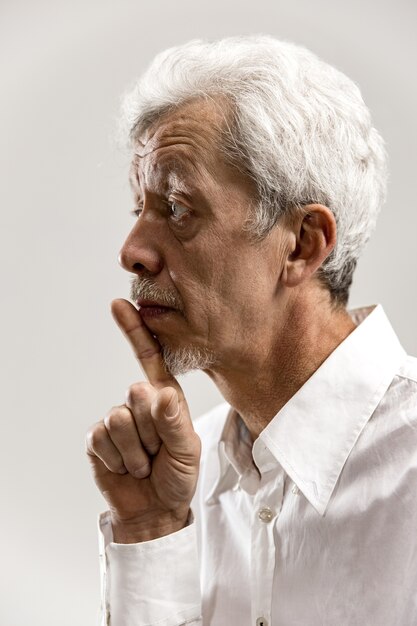 Homem sênior sério e assustado mantém o dedo da frente nos lábios, tenta manter a conspiração, diz: Shh, faça silêncio, por favor. Foto isolada de homem mostrando gesto de silêncio