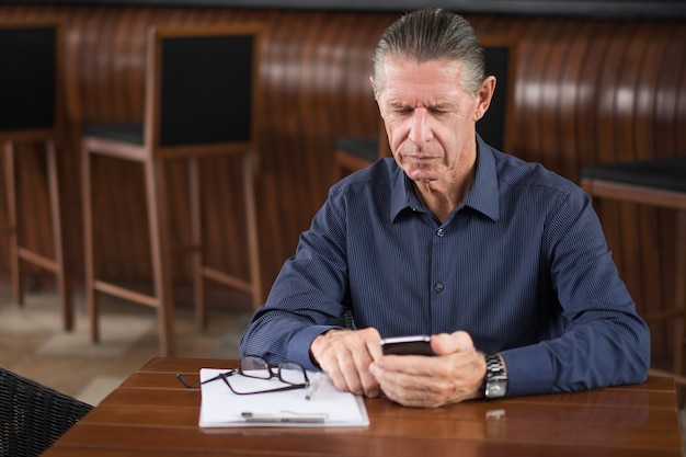 Homem sênior sério que lêem a mensagem no telefone no café