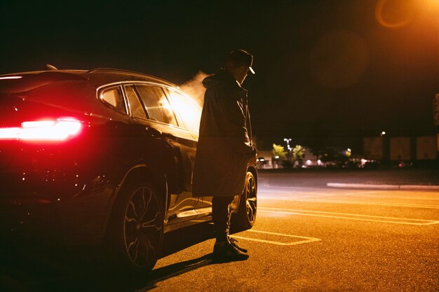 Homem sentado ao lado do carro à noite