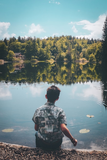 Homem sentado em frente a um lago sob um céu azul