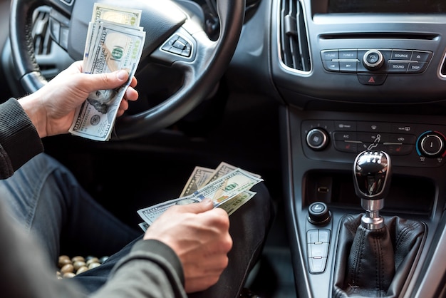 Homem sentado em um carro contando notas de dólar para ou como suborno, seguro ou crédito, investindo. vender ou alugar carro