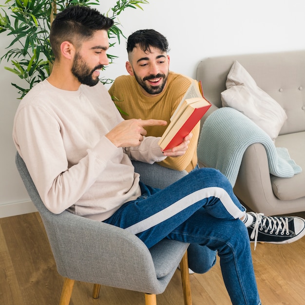 Foto grátis homem sentado na cadeira mostrando algo no livro para seu namorado