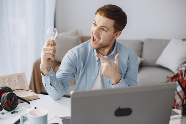 Homem sentado na sala de estar em casa. Cara gostando de estudar usando laptop e fone de ouvido. O homem tem uma ideia.