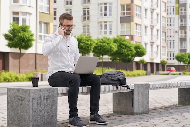 Homem sentado no banco trabalhando no laptop falando por telefone