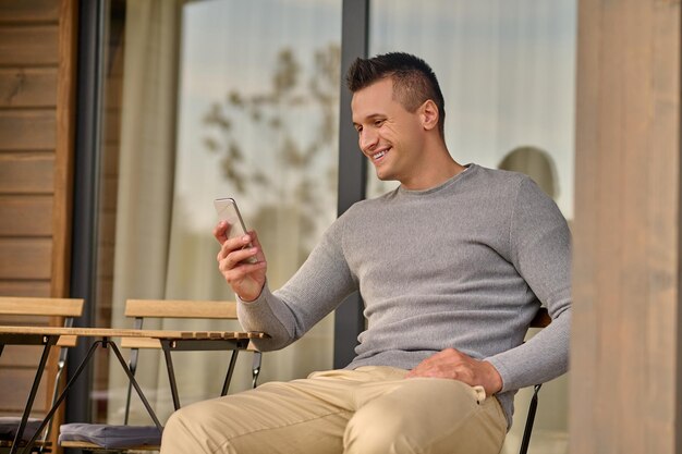 Homem sentado perto de casa de campo olhando para smartphone