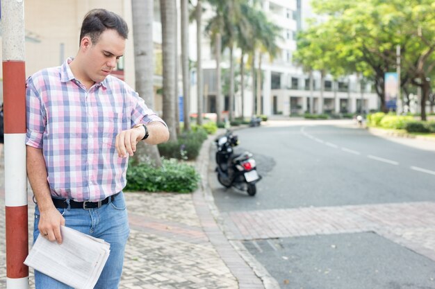 Homem sério com jornais que controlam o tempo na rua