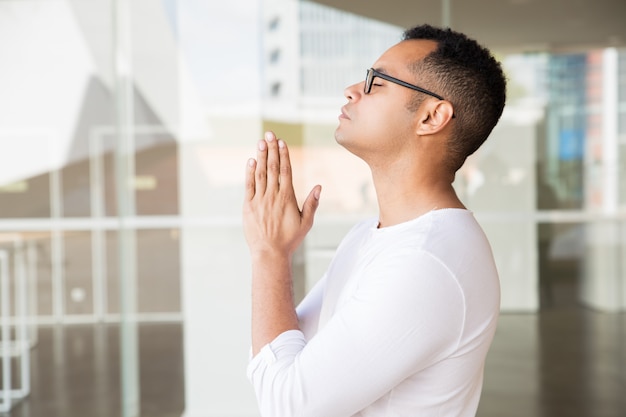Homem sério com os olhos fechados, colocando as mãos em posição de oração