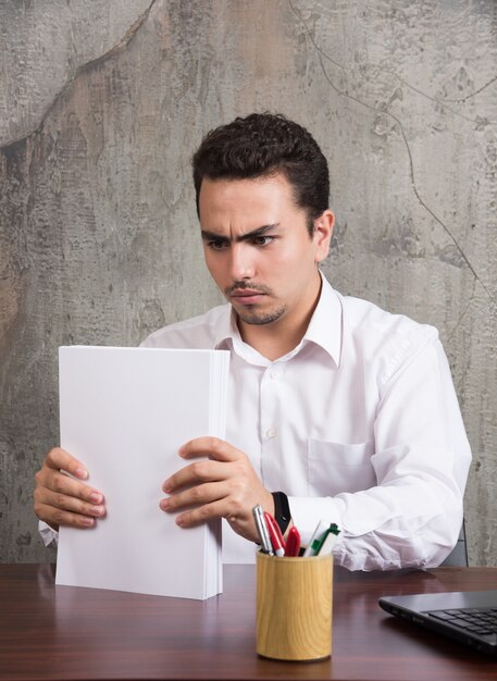 Foto grátis homem sério, segurando folhas de papel e sentado à mesa.