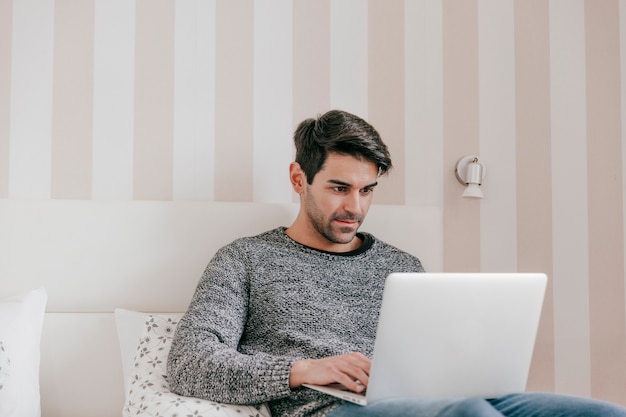 Homem serio usando laptop na cama