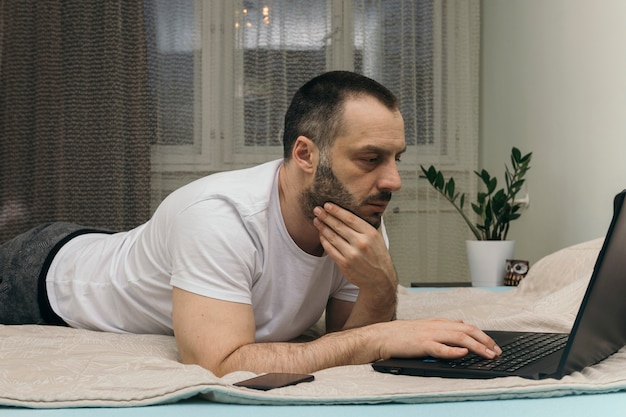 Homem sério usando laptop na cama