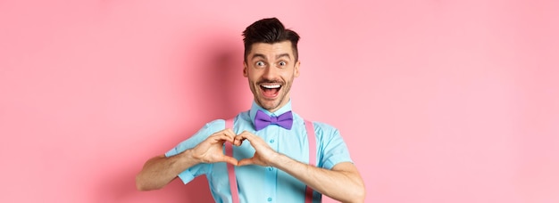 Foto grátis homem sorridente animado mostrando o coração batendo e olhando com amor parado sobre o backgro rosa romântico