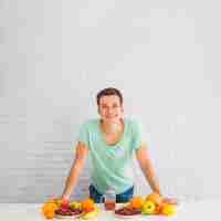 Foto grátis homem sorridente, apoiando-se na mesa com muitas frutas coloridas