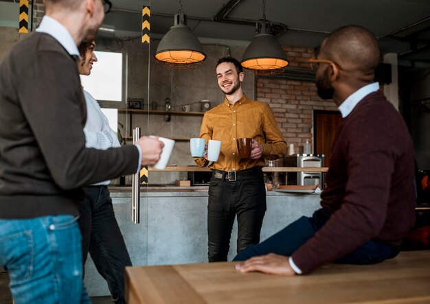 Homem sorridente carregando canecas com café para os colegas
