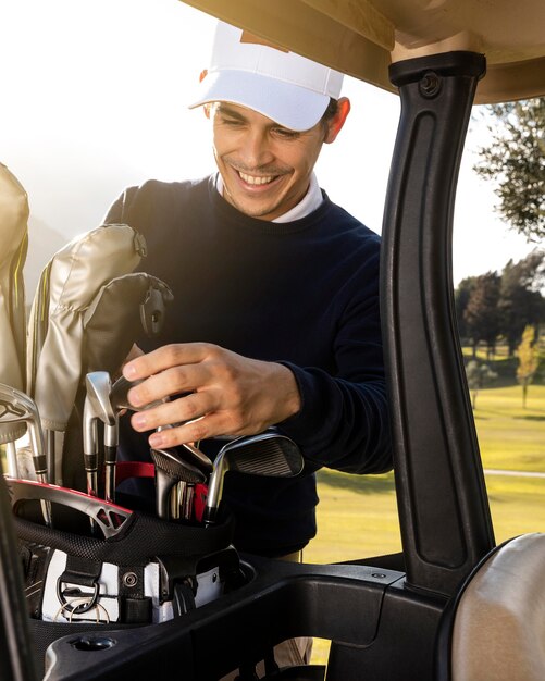 Homem sorridente colocando tacos no carrinho de golfe