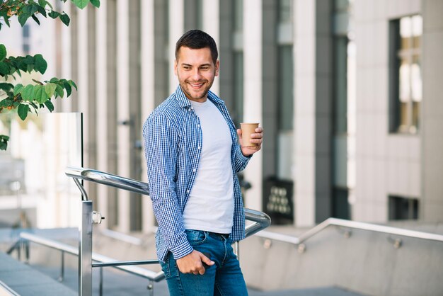 Homem sorridente com café perto do corrimão