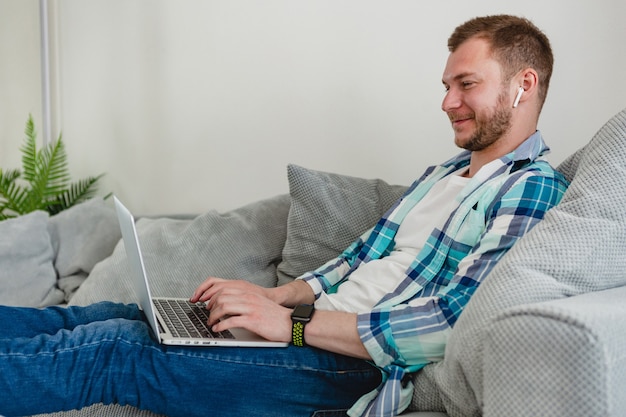 homem sorridente com camisa sentado relaxado no sofá em casa à mesa trabalhando online no laptop de casa