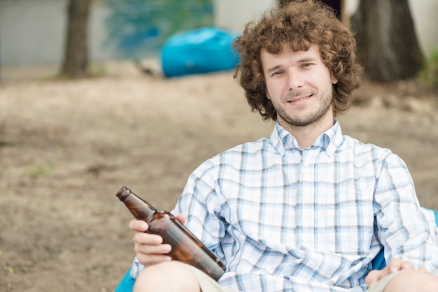 Homem sorridente com cerveja relaxante na praia