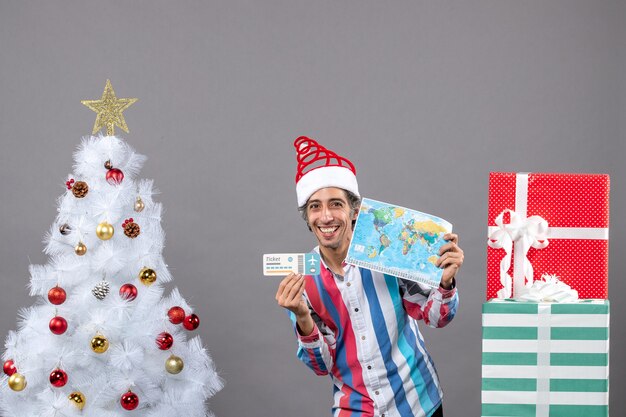 Homem sorridente com chapéu de papai noel segurando um mapa-múndi e uma passagem