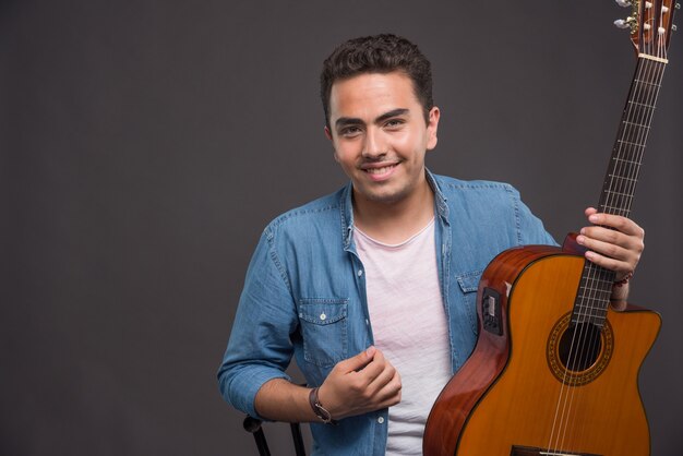 Homem sorridente com guitarra sorrindo em fundo escuro.