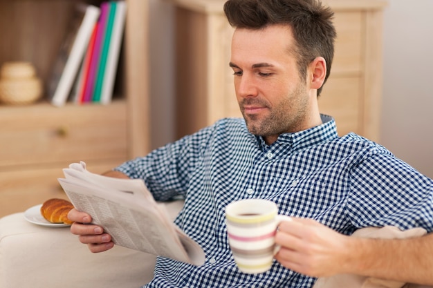 Homem sorridente com jornal e xícara de café