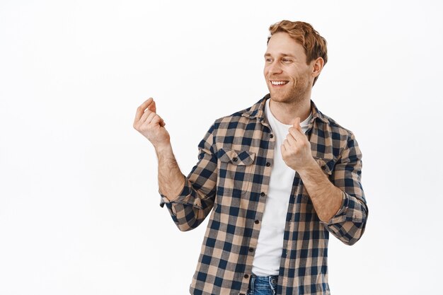 Homem sorridente dançando e estalando os dedos e se divertindo, dançando e parecendo feliz, vire a cabeça para o texto promocional do logotipo, em pé sobre a parede branca