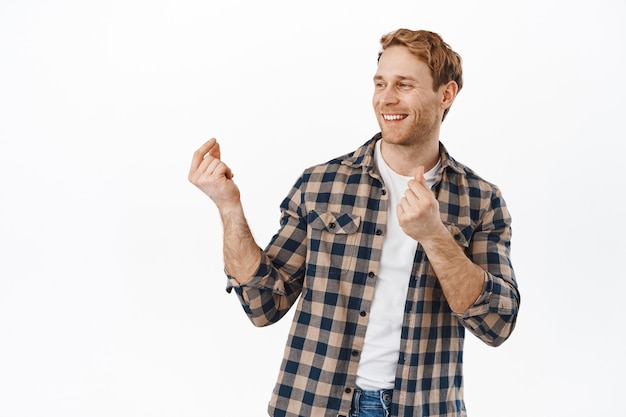 Homem sorridente dançando e estalando os dedos e se divertindo, dançando e parecendo feliz, vire a cabeça para o texto promocional do logotipo, em pé sobre a parede branca