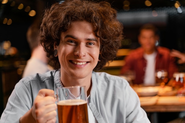 Homem sorridente de close-up segurando uma caneca de cerveja no bar