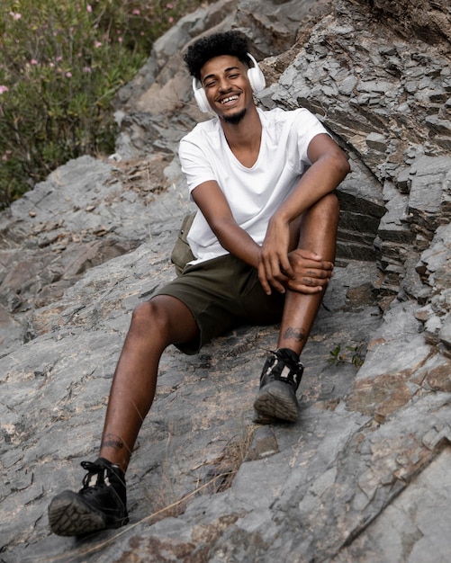 Homem sorridente de foto completa sentado na rocha