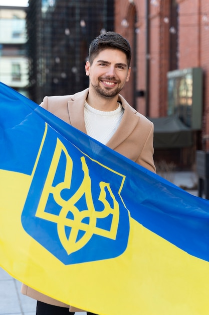 Foto grátis homem sorridente de tiro médio segurando a bandeira ucraniana