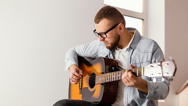 Homem sorridente de tiro médio tocando guitarra dentro de casa