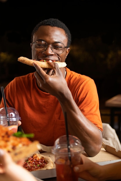 Homem sorridente de vista frontal comendo pizza