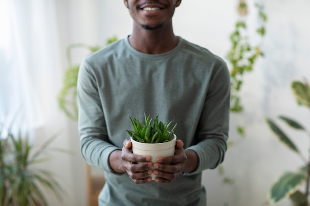 Foto grátis homem sorridente de vista frontal segurando o vaso de plantas