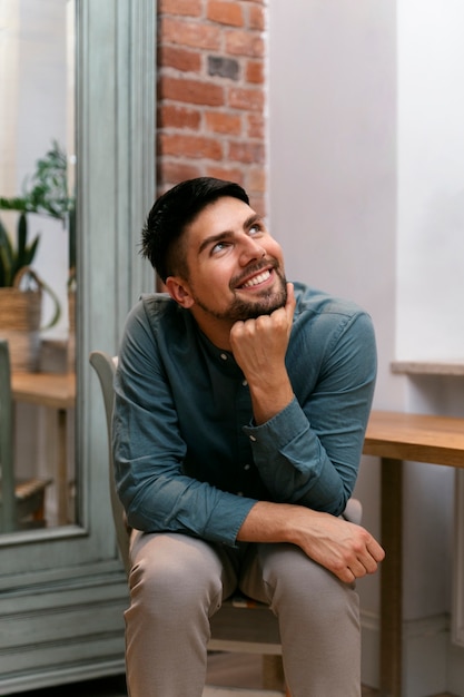 Homem sorridente de vista frontal sentado dentro de casa