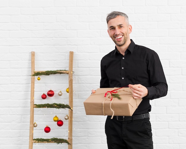 Homem sorridente desembrulhando um presente ao lado de uma escada com objetos de Natal