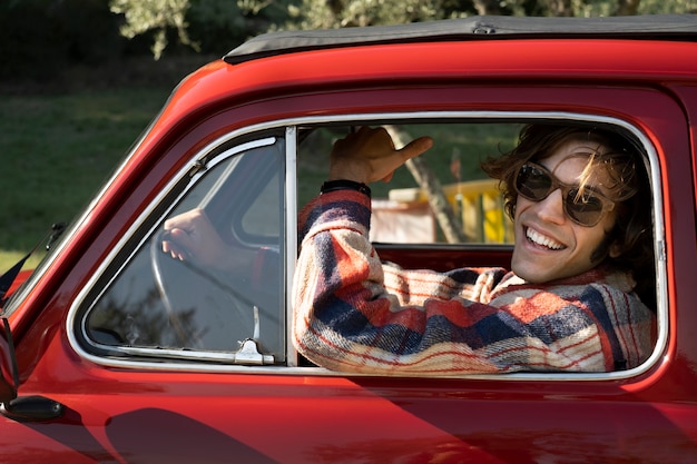 Homem sorridente dirigindo carro vermelho de perto