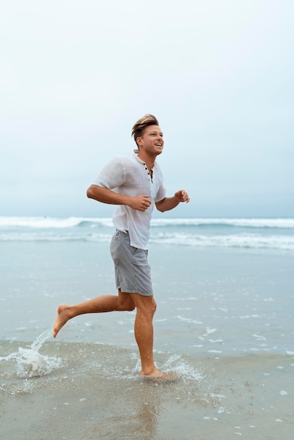 Homem sorridente em cena completa correndo na praia