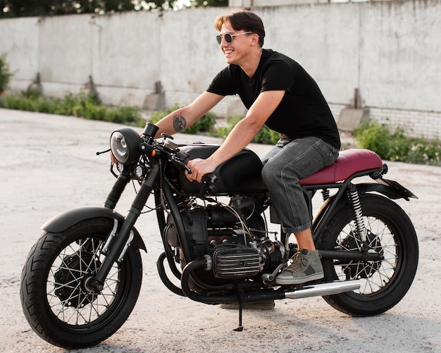 Homem sorridente em foto completa posando em uma motocicleta