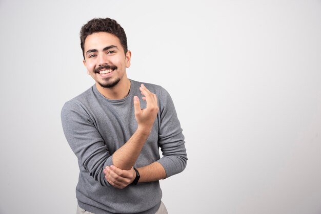 Homem sorridente em pé e posando sobre uma parede branca.