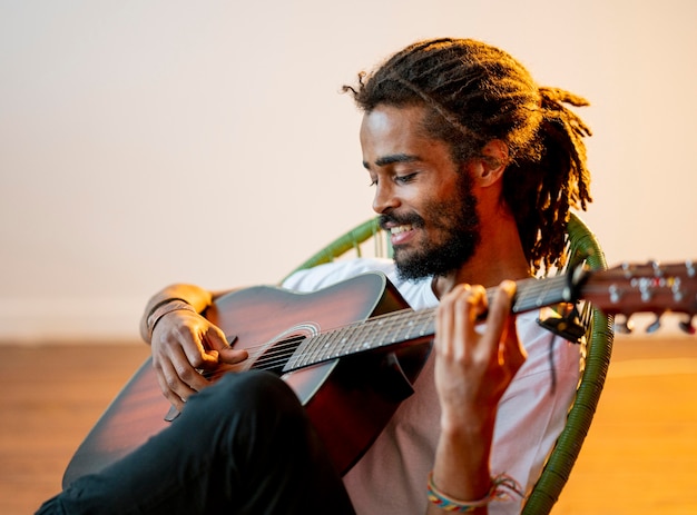 Homem sorridente lateralmente com dreads tocando guitarra